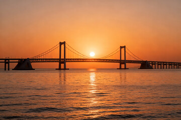 Sunset over a suspension bridge spanning a calm body of water