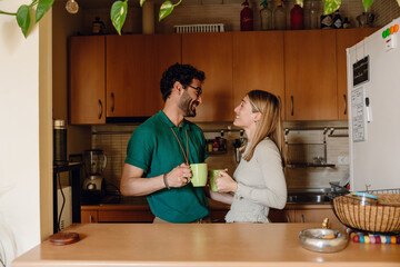 A man and a woman stand and look at each other while laughing and holding cups