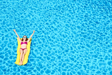 Young woman on inflatable mattress in swimming pool, above view