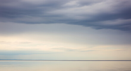 Obraz premium Dramatic overcast sky with soft light reflecting on a calm expansive body of water