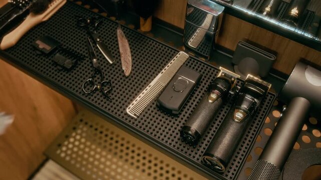 Close-up of hand of anonymous young male barber picking up comb from tray with tools at hair salon, while preparing to do haircut. Scissors, trimmer, shaver, hairdryer on shelf under mirror