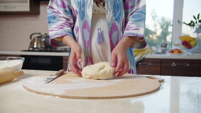 Woman in ethnic clothing dropping dough on wooden board