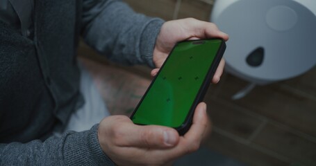 Businessman Sitting on the Toilet, Using Smartphone with Green Screen. Man Feeling Relaxed in Restroom in Modern Office During Work. Template for Media Content. Lifestyle and Daily Routine. Close Up.