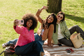 Fototapeta premium A group of three female friends are posing on a blanket and smiling while looking at a phone that one of them is holding