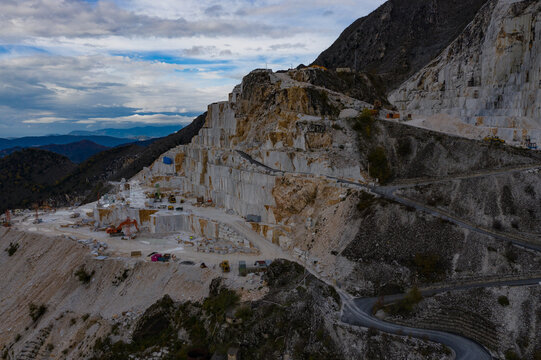 Aerial view of the stark white marble quarries cascading down the rugged mountain slopes under a cloudy sky, Carrara, Tuscany, Italy.