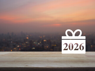 Gift box happy new year 2026 flat icon on wooden table over blur of cityscape on warm light sundown, Business shop online concept