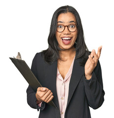 Latina businesswoman holding a report receiving a pleasant surprise, excited and raising hands.