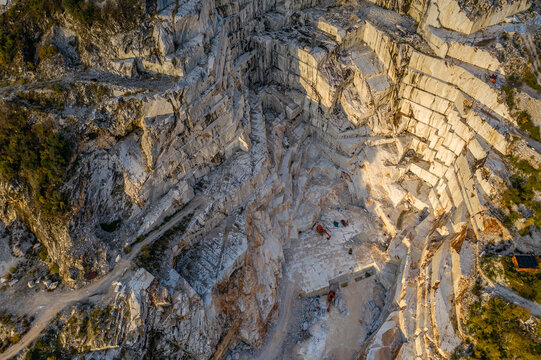 Aerial view of raw, jagged marble terraces cascade down the mountainside, scarred by quarrying, revealing the stark beauty of Carrara's stone, Carrara, Tuscany, Italy.