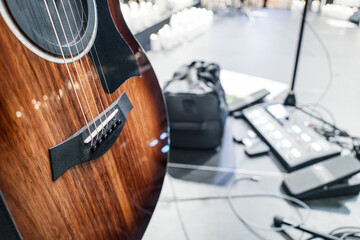 High quality, wooden acoustic guitar seen on its stand, on a stage during rehearsals at a gig in Britain. Electronic amp floor pedals can be seen on the stage floor.