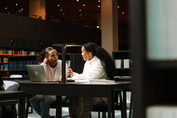 A female student listens to a female student sitting next to her at a table and talking