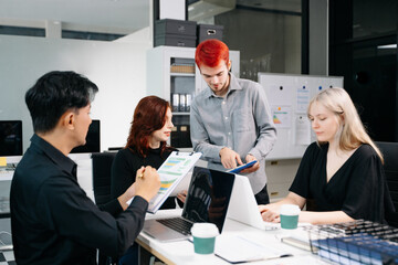 Diverse business team collaborating in a meeting with laptops, tablets, and reports, symbolizing...