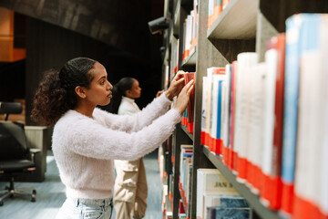 A female student looks at a book she takes out from the bookshelf