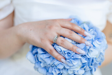 Beautiful bride holding blue hydrangea bouquet with wedding ring visible