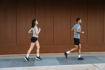A female athlete runs after a male athlete near a wall