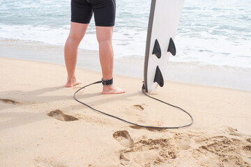 A surfboard fastened to a man's feet on the beach in the sand, close-up view from behind.