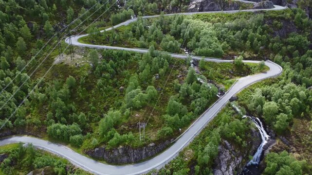 Aerial view of the winding Lysevegen road snaking through lush green trees and rocky terrain, creating a striking contrast, Lysebotn, Rogaland, Norway.