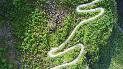 Aerial view of the winding Lysevegen road snaking through lush greenery, adjacent to a cliff and a waterfall, creating a striking contrast of colors, Lysebotn, Rogaland, Norway. - Powered by Adobe