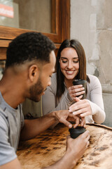 A female athlete laughs while holding her hand near a male athlete who sits next to her at a table while they hold cups