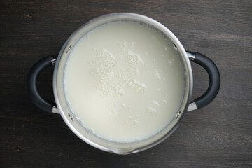 Metal saucepan with fresh white milk on wooden table in the kitchen, closeup, top view
