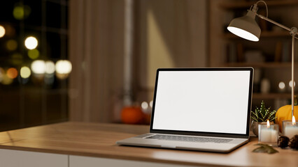 White screen laptop with pumpkin and aroma scented candle aside lamp on wooden table in dim lit room