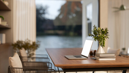 Fototapeta premium White screen laptop with book and glasses aside vase on wooden table with metal chair in living room