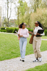 A female student is holding a folder and talking to a female classmate who is walking next to her...
