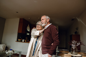 A man and a woman are hugging and looking ahead while she smiles