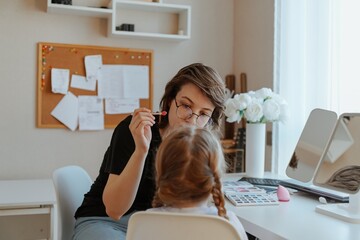 A young mother and her 3-year-old daughter play dress-up as makeup artists, sharing laughter and...
