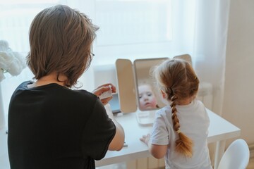 A young mother and her 3-year-old daughter play dress-up as makeup artists, sharing laughter and...