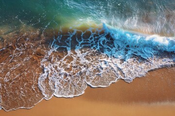 Aerial view of a powerful ocean wave crashing onto a sandy beach with white foam and clear blue water