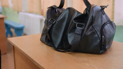 Close up of black bag being dropped on wooden table while strap is adjusted by person in sportswear, capturing preparation moment and detail of equipment handling in indoor environment