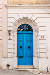 Elegant traditional Maltese townhouse facade with a bright blue wooden door, arched frame, decorative ironwork, and vintage knocker details
