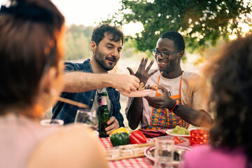 Happy male friends talking and smiling at a summer barbecue party. Man sharing food in a candid...