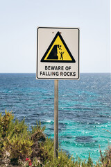 Warning sign on a rocky coastal trail between Marsaskala and Marsaxlokk, Malta, cautioning about falling rocks with a clear blue sea in the background