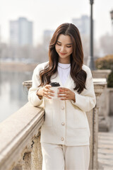 Fototapeta premium A young woman enjoying the scenery in the park, holding a coffee cup