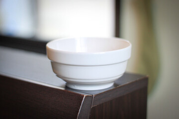 A clean white ceramic bowl placed on a wooden surface with natural light coming from the window. The simple and minimal design highlights elegance, functionality, and everyday household use. © payut