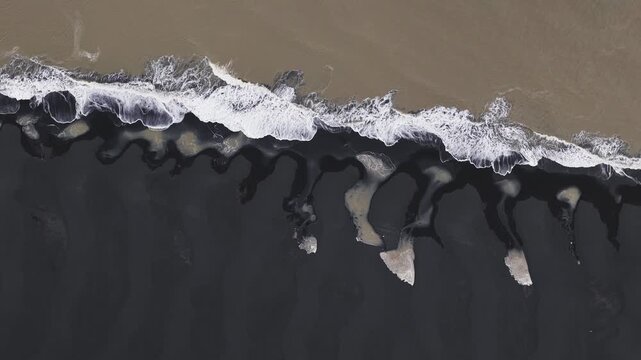 Aerial view of the stark contrast between the white foamy waves and the black sand beach, creating a dramatic coastal scene, Clyne Castle, Iceland.