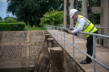 Fototapeta premium A male dam engineer is checking the water volume in the reservoir and recording it in a document