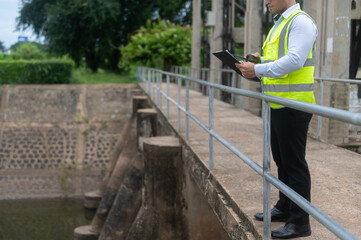Fototapeta premium A male dam engineer is checking the water volume in the reservoir and recording it in a document