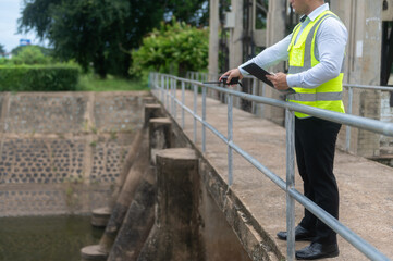 A male dam engineer is checking the water volume in the reservoir and recording it in a document