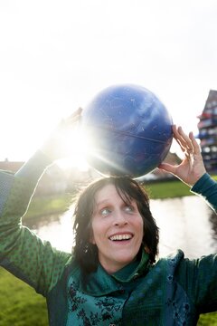 Smiling woman balancing astrological globe on head in sunny park