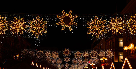Festive street decorations with glowing snowflake lights hanging above city street at night....