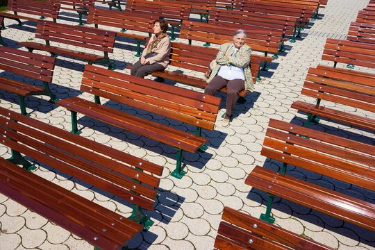 Women sitting apart on empty benches outdoors with visible tension