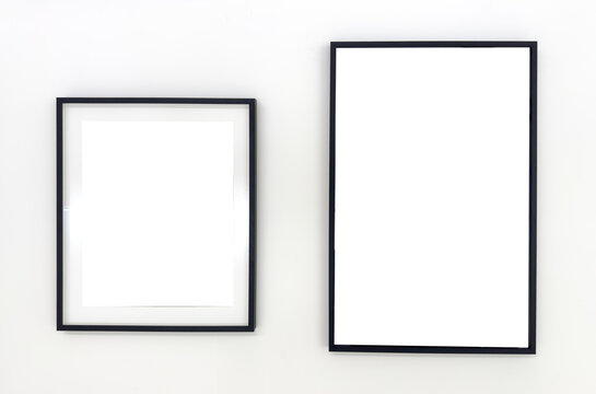 Two empty black photo frames of different sizes hanging on a white wall. Minimalist mockup for
