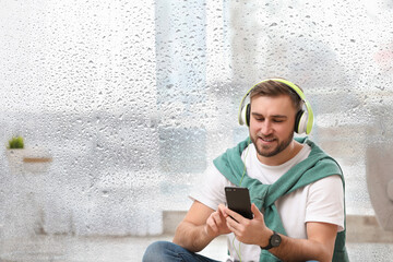 Happy man listening to sounds of nature which making him feel calm. Double exposure of room and wet window on rainy day