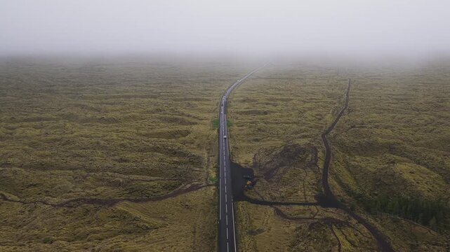 Aerial view of a dark asphalt road cutting through a vast expanse of mossy lava field under a blanket of mist, G&ouml;ngulei&eth; um Eldhraun, Skaft&aacute;rhreppur, Iceland.