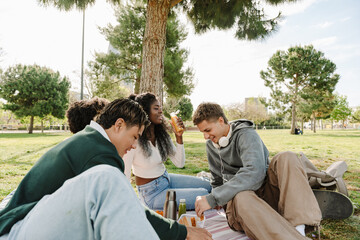 A group of four students are smiling and sitting on a blanket while one of them holds a bottle
