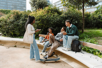 A female student stands and holds a phone while listening to a group of three students sitting across from her and smiling