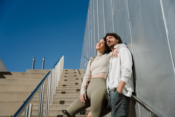 Male and female athletes hug and smile while standing on stairs and leaning on a wall