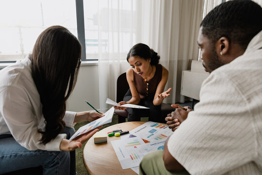 A group of three workers are sitting at a table while two of them are looking at charts